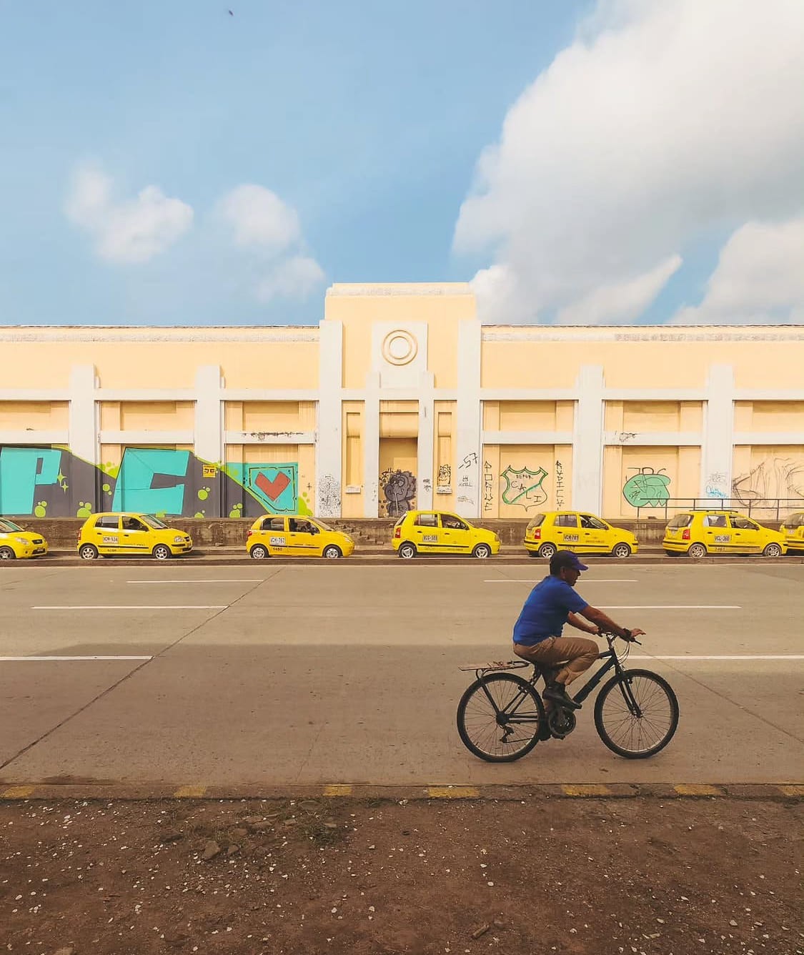 Taxis amarillos y un ciclista frente a una fachada art déco de Cali